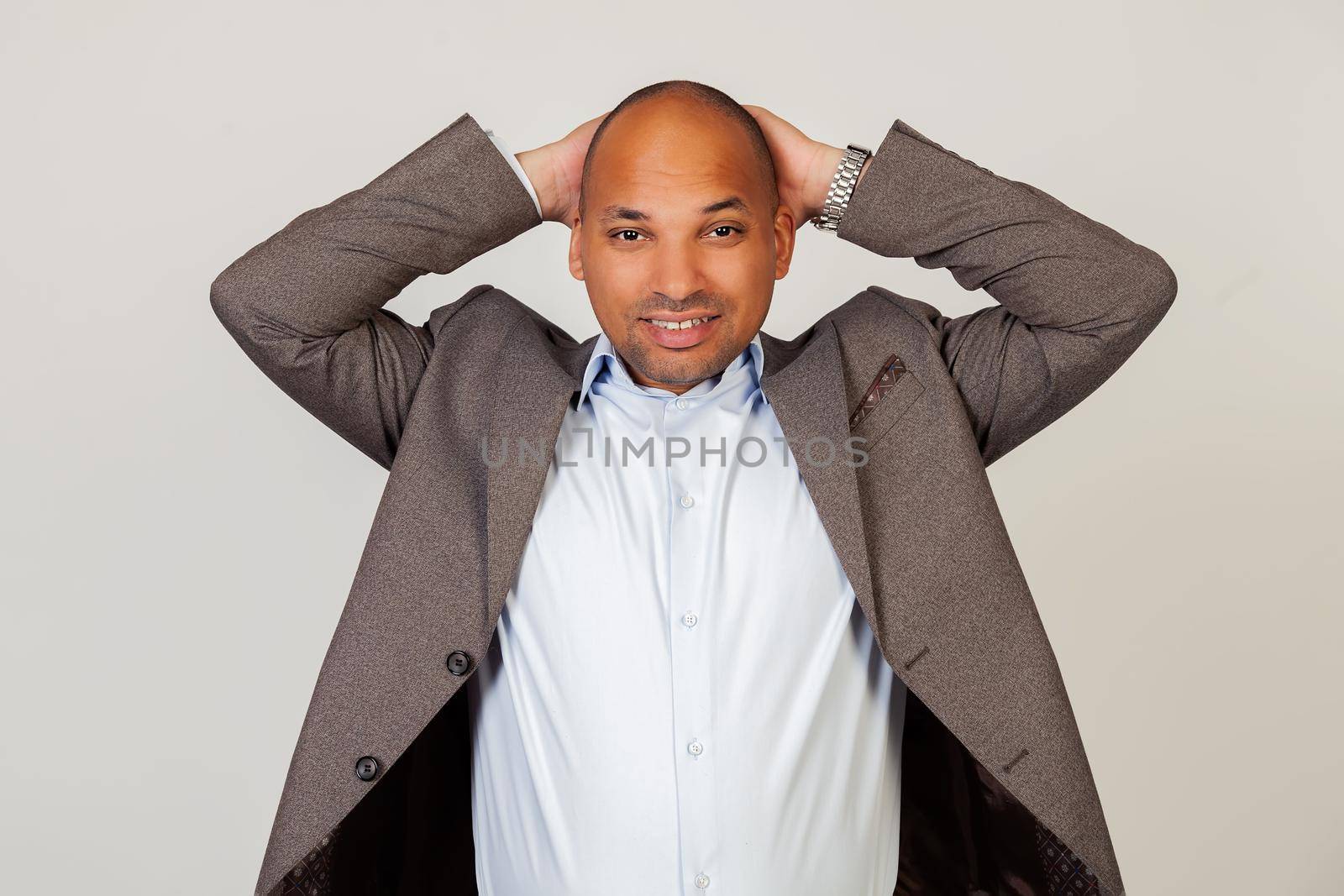 Portrait of an upset young African American guy businessman looking at the camera holding hands in his head. Standing on a gray background