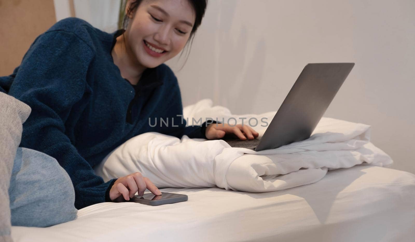 Portrait of an Asian woman lay down Playing Modern Technology phone in bed. Concept. Working at home..