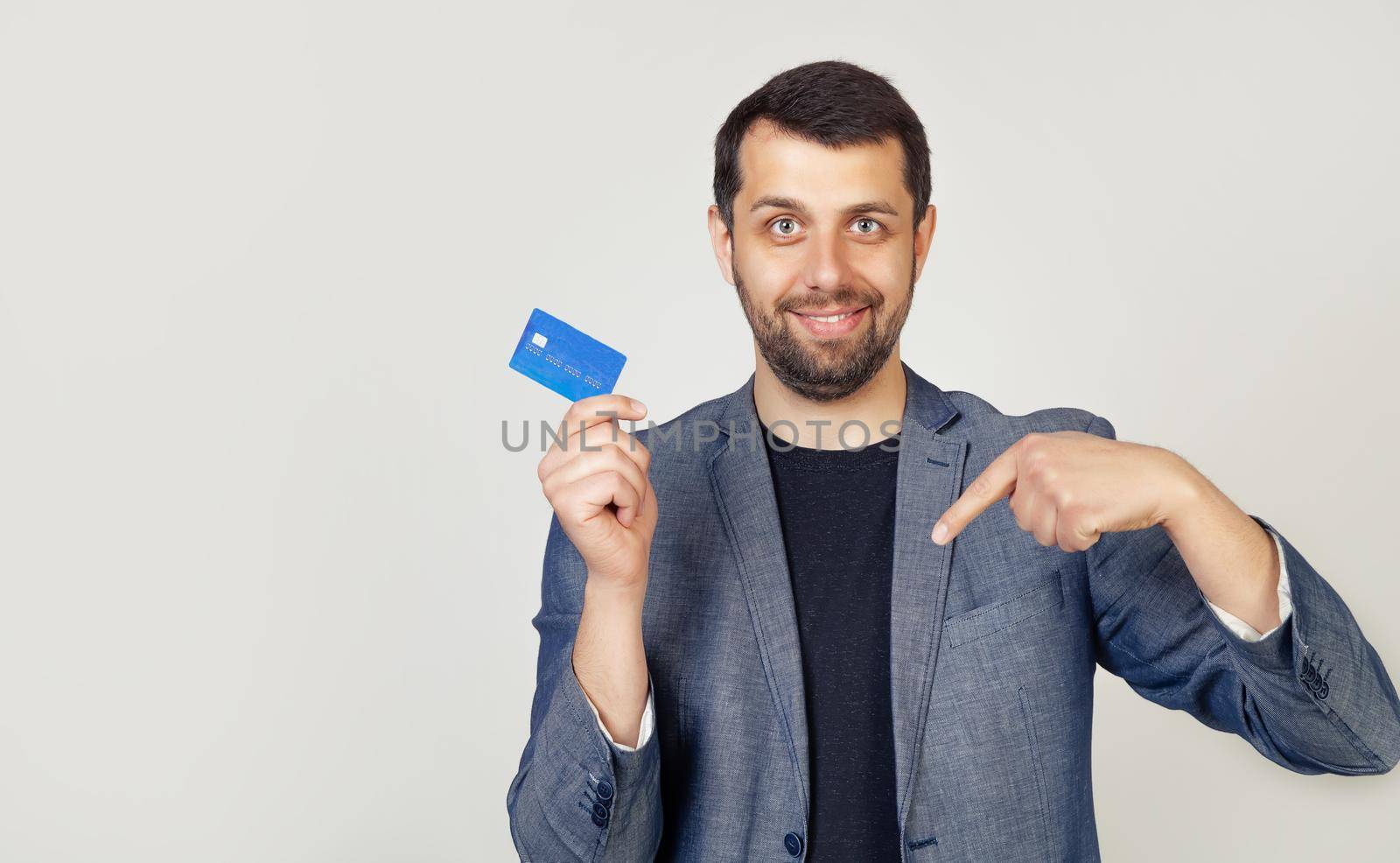 Young businessman man with a beard a bank customer holding a credit card, standing on a white background with a happy face, pointing his finger to the bottom of the link
