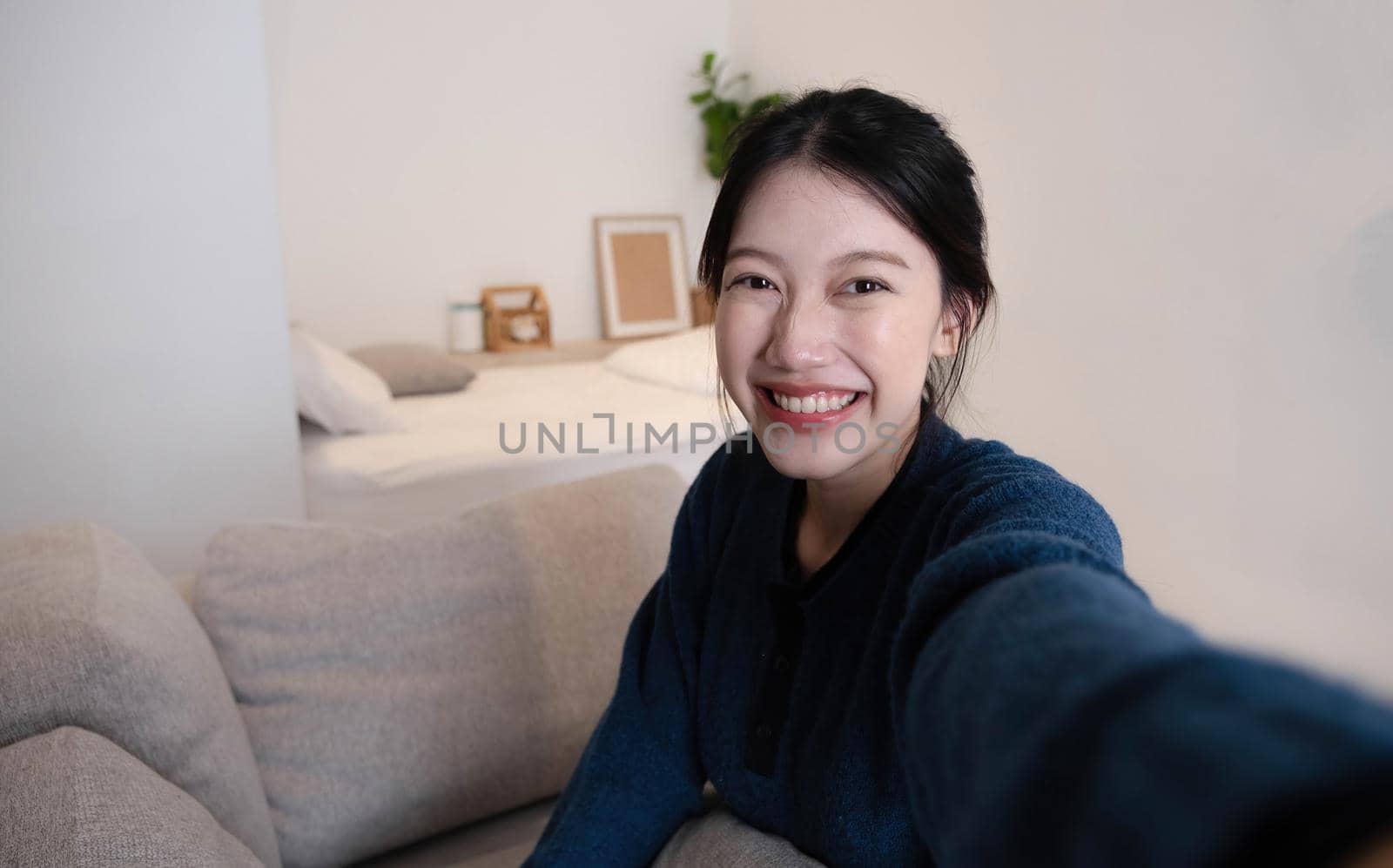 Portrait of Young Asian woman video call with her friend and checking social media by smartphone sitting on couch. Lifestlye concept. by wichayada