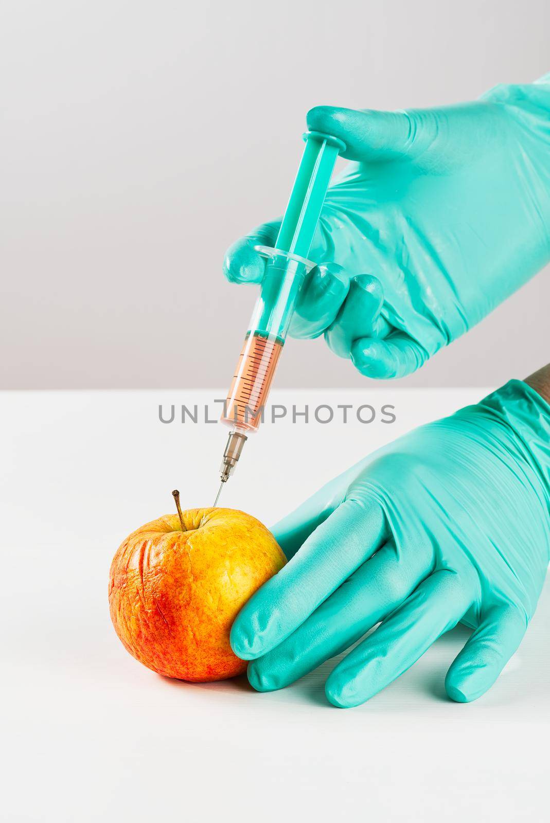A hand in a medical glove inserts a syringe into apple. Harmful food additives. GMOs Concept by PhotoTime
