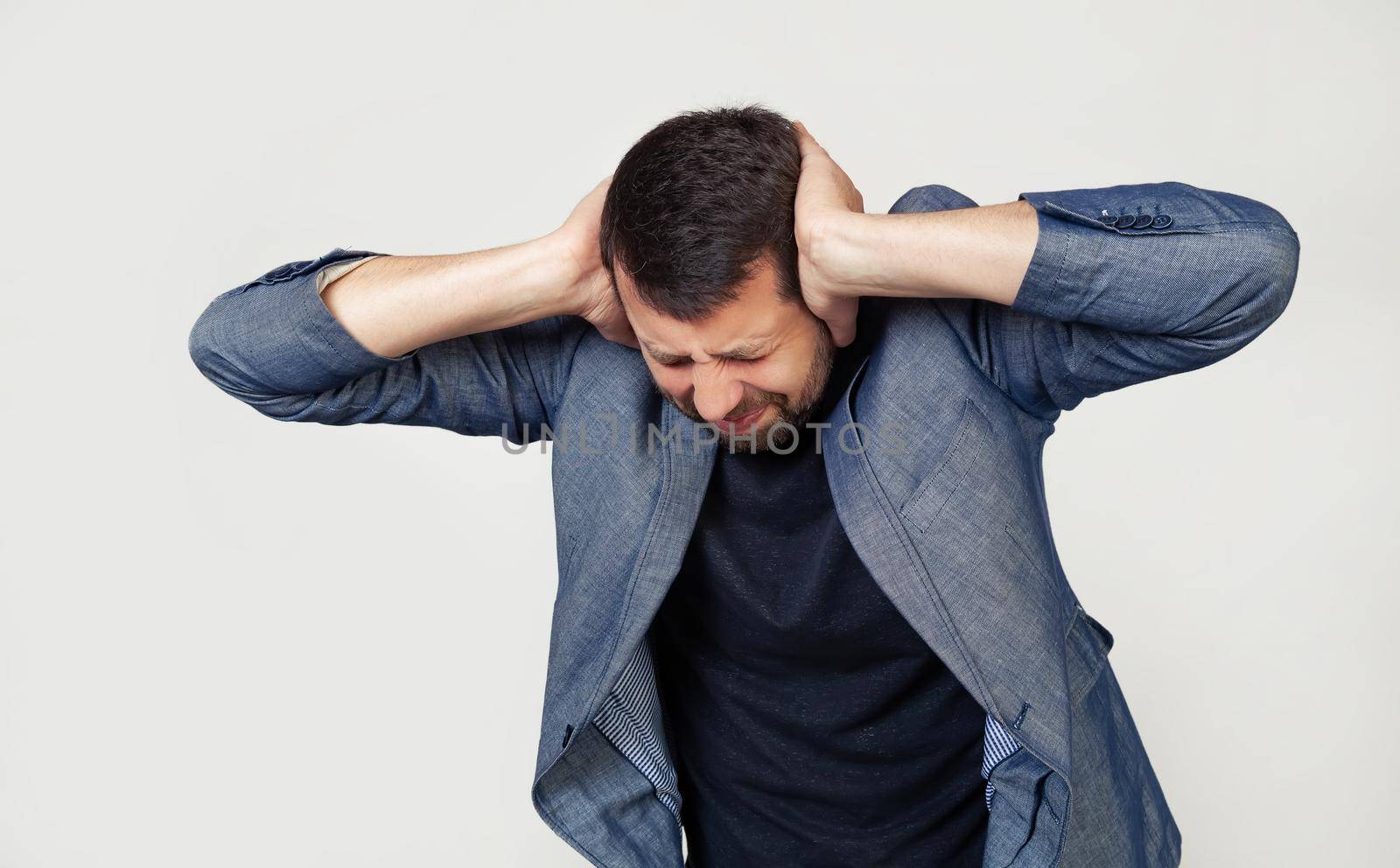 Young businessman man with a beard in a jacket. Hands on head, suffering from headache in despair and under stress due to pain and migraine. Portrait of a man on a gray background by ViShark