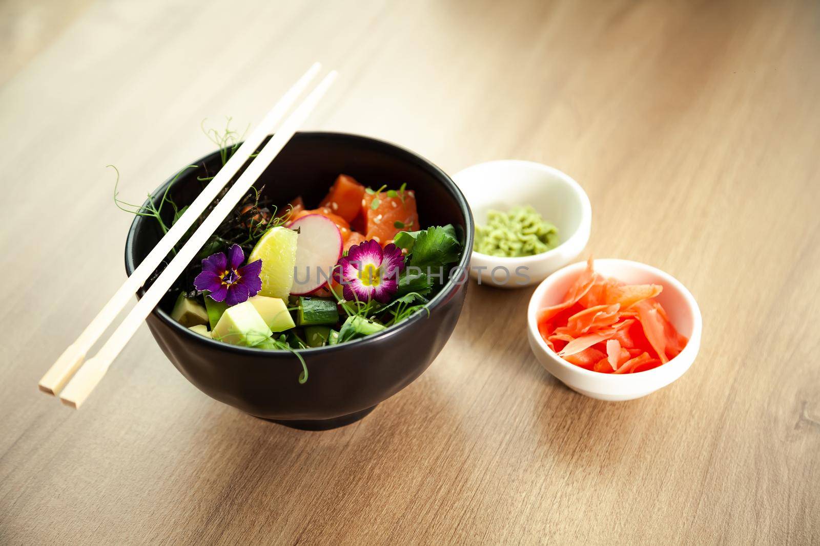 Poke salad with salmon in a bowl next to wasabi and ginger. Ingredients fresh salmon, avocado, cucumber, rice, Tamarind sauce mango sauce nori lime, sesame seeds, cilantro. Asian seafood salad concept