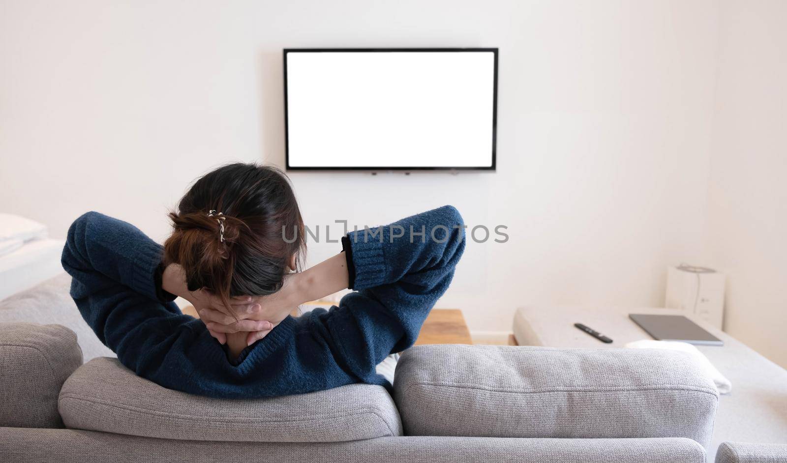 behind of asian young woman watching white screen TV on the sofa at home by wichayada