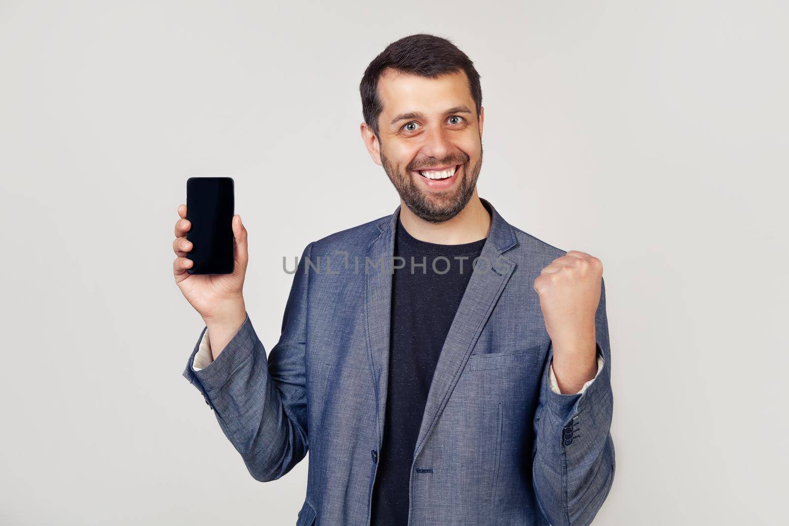 Young man showing smartphone screen on an isolated background screaming proud and celebrating victory and success is very excited, encouraging emotions. 5G communication technology