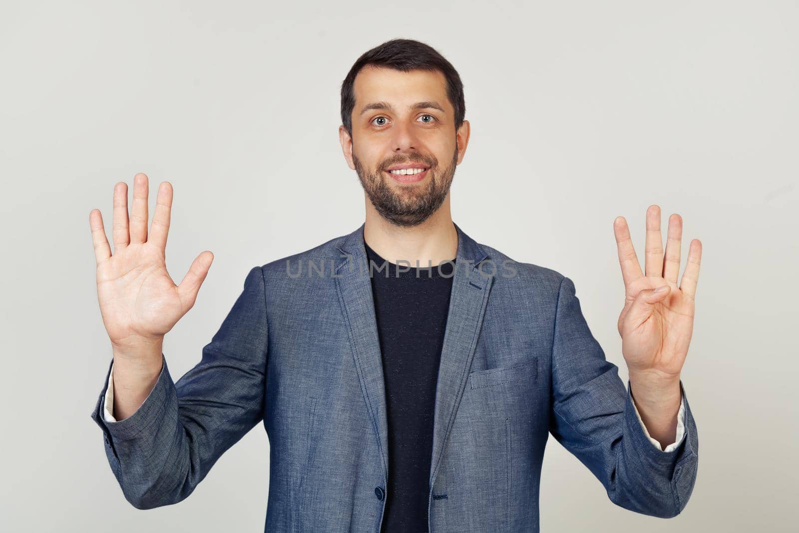 Young businessman man with beard smiling, showing number nine with fingers on hand, smiling confidently and happily, looking into the camera. The man shows nine fingers. Number 9.