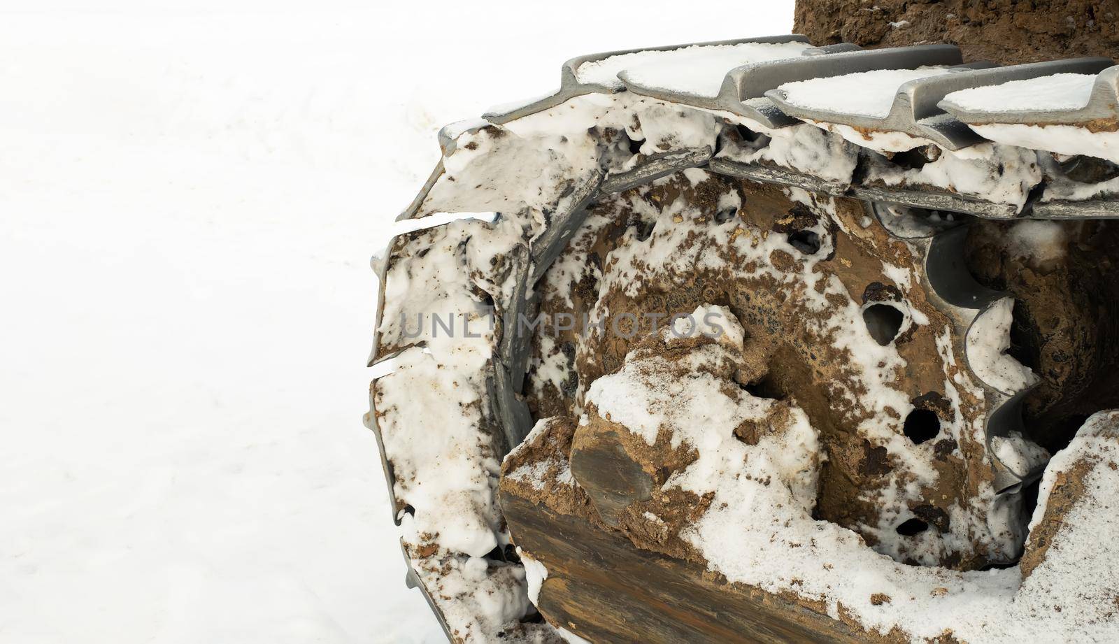 The metal tracks of a bulldozer tractor in winter clears the road from snow. On a frosty day, a yellow bulldozer in winter