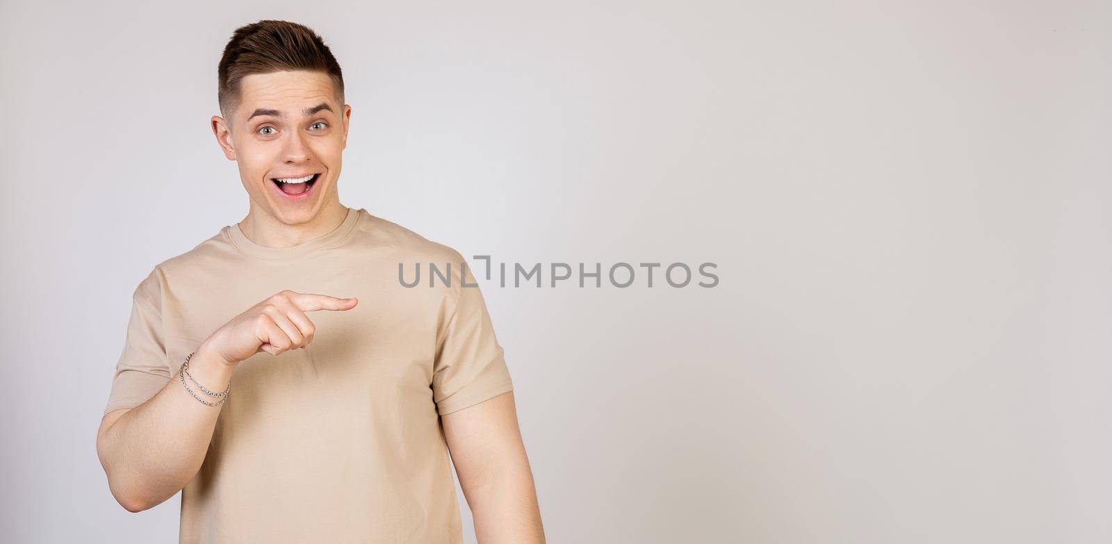 The man points to the side and smiles. Photo of young attractive excited handsome modern freelancer, entrepreneur, employer student looking at camera, pointing with index finger to copy space.