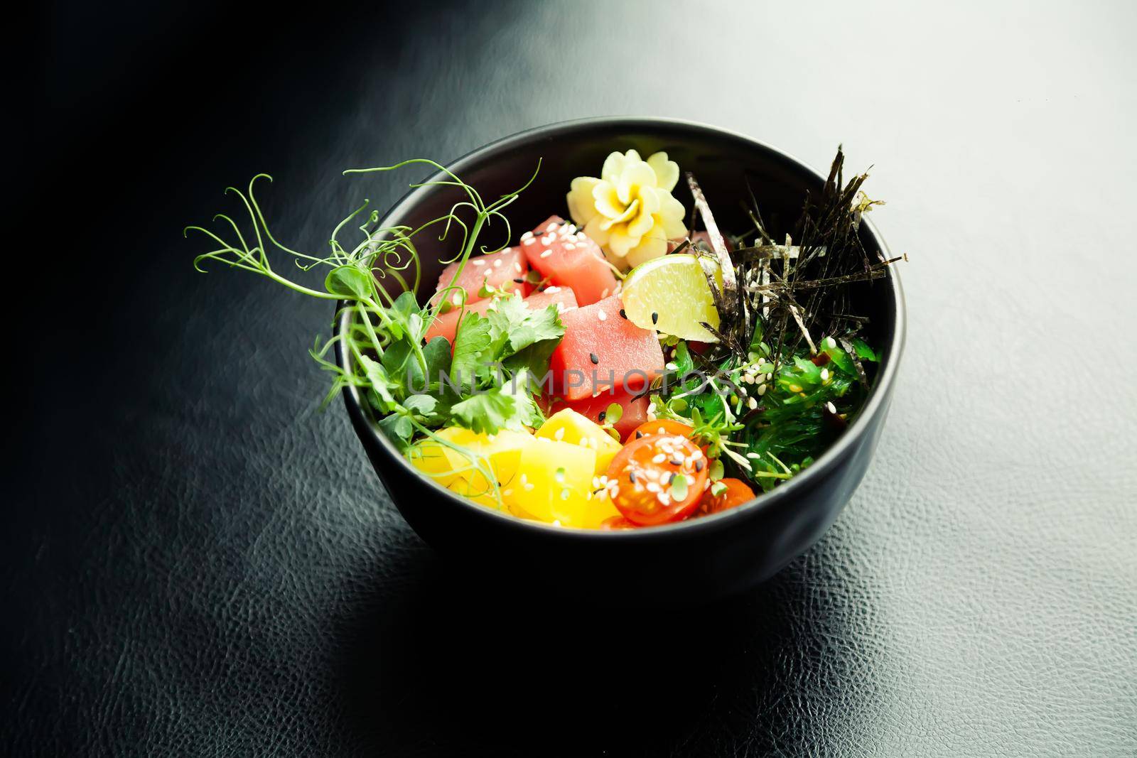 Poke salad with tuna in a bowl. Ingredients fresh tuna, cherry tomatoes, marinated seaweed, rice, takuan, Ponzu sauce, Teriyaki sauce, nori, sesame seeds, lime, cilantro. Asian seafood salad concept
