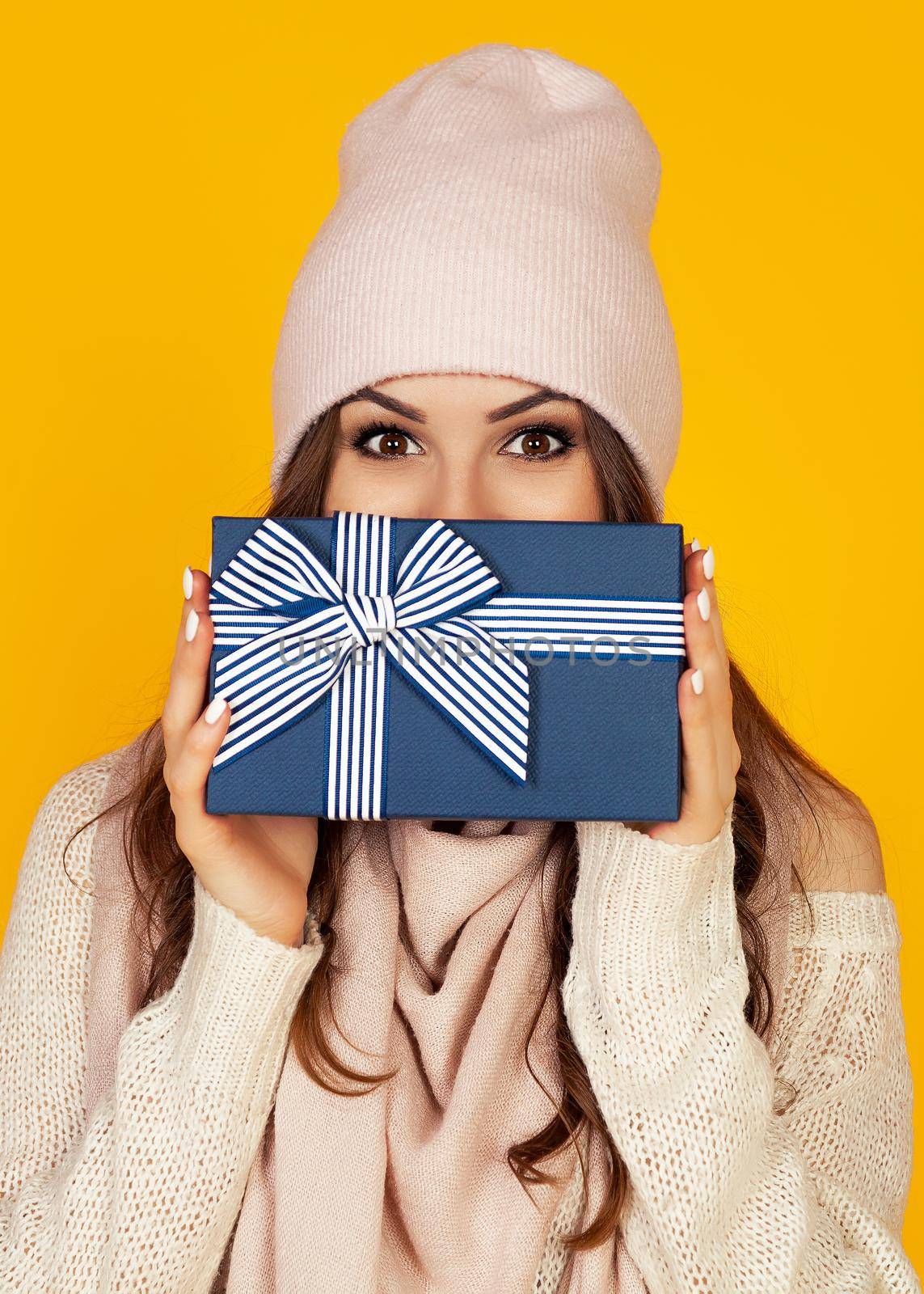 Happy young woman with a gift box in her hands, covers half of her face with a New Year's gift. The girl shows a gift to the camera. The concept of gifts and surprises for the new year and christmas.