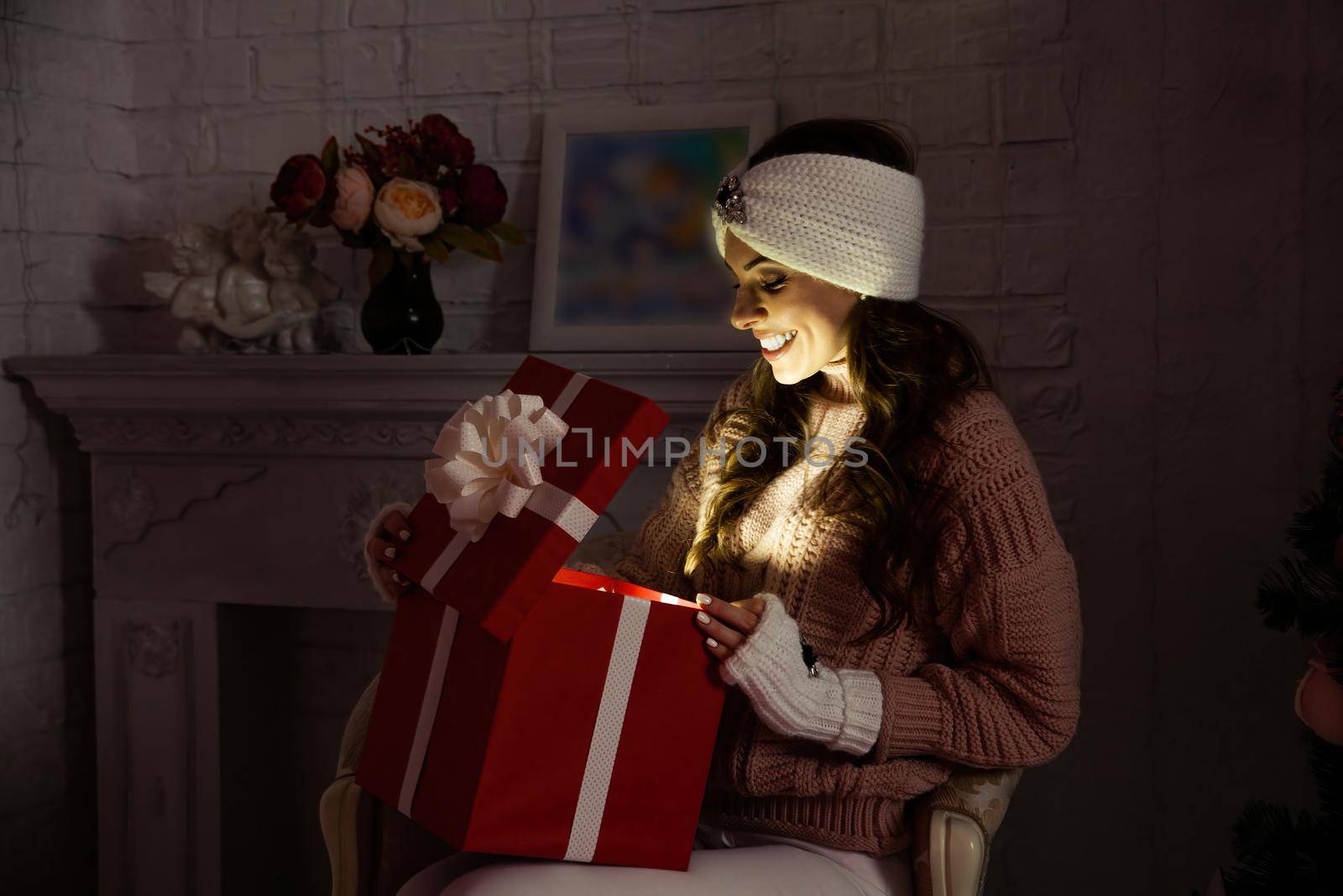 Happy young woman with a present, opening a Christmas present box. Portrait of happy smiling girl opening gift box isolated on red background. by ViShark
