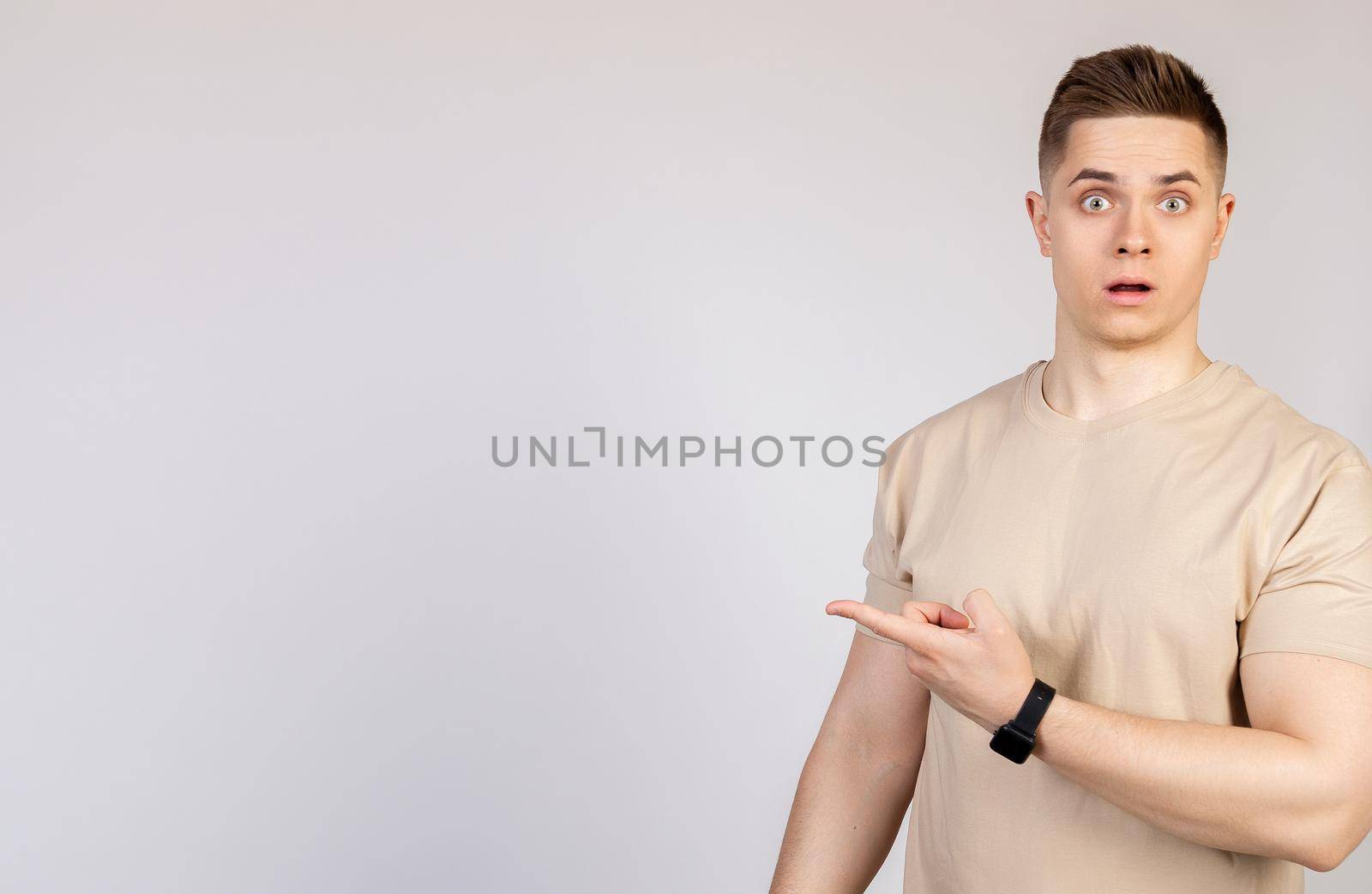 The man the guy points to the side with a displeased face. Young doubter man, holds his hand and points to the side with forefingers at blank space