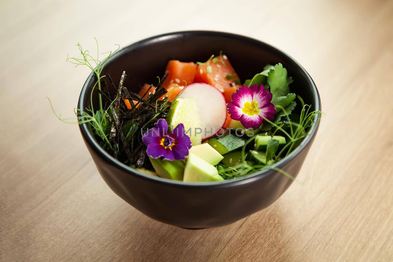 Poke with salmon in a bowl. Ingredients fresh salmon, avocado, cucumber, rice, Tamarind sauce, mango sauce, nori, lime, sesame seeds, cilantro. Seafood concept. Asian salmon poke salad.