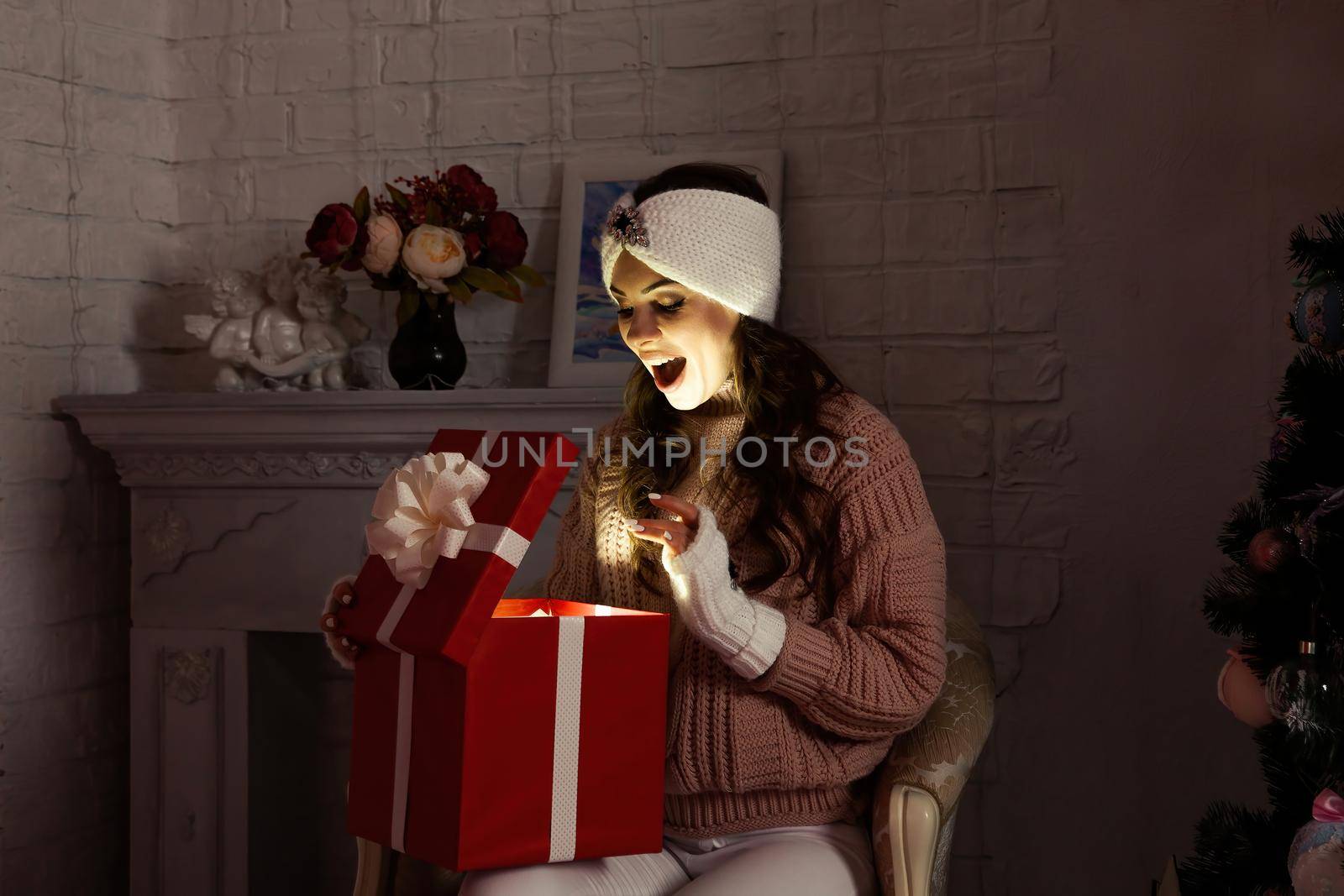 Happy young woman with a present, opening a Christmas present box. Portrait of happy smiling girl opening gift box isolated on red background