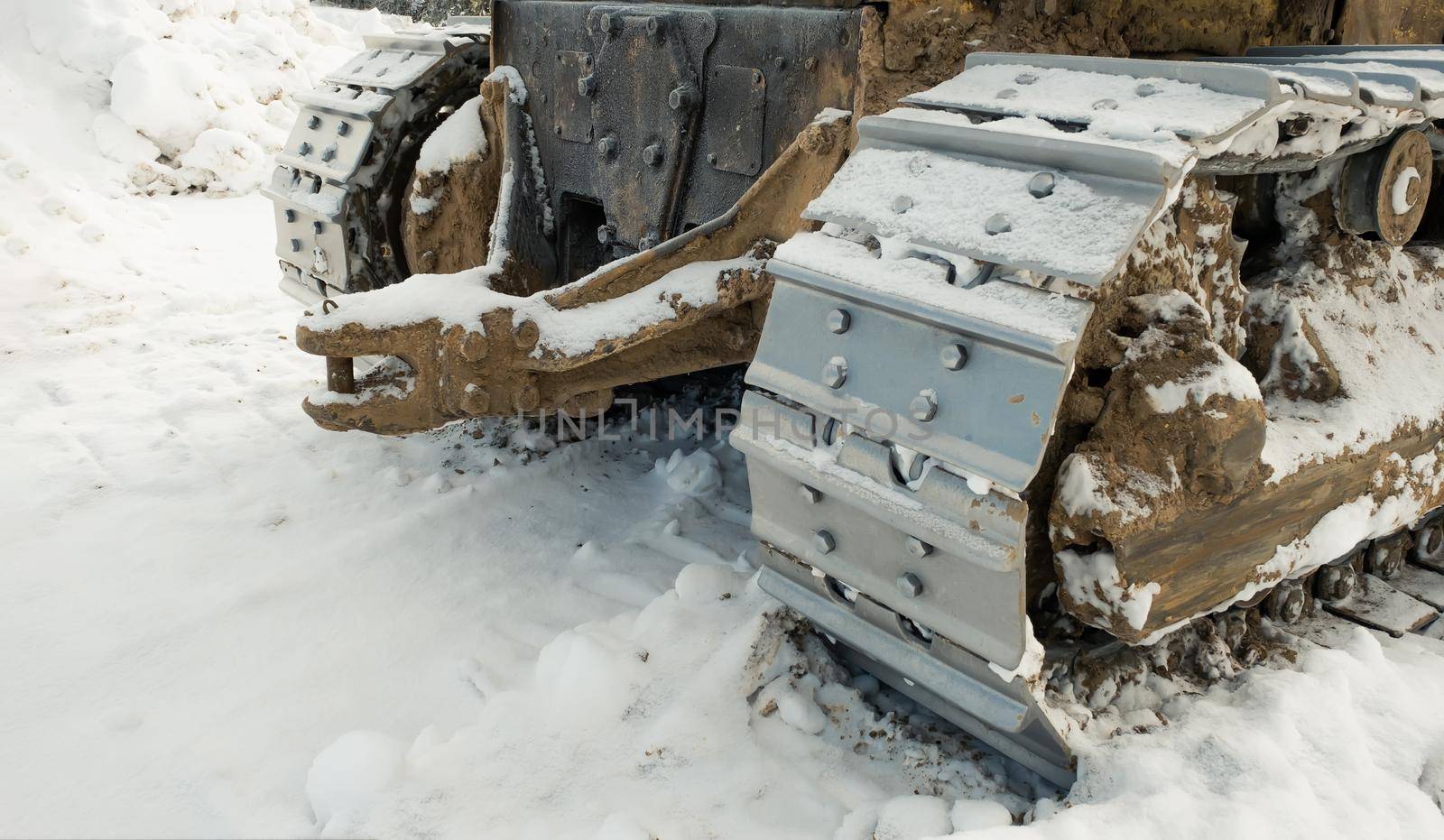The metal tracks of a bulldozer tractor in winter clears the road from snow. On a frosty day, a yellow bulldozer in winter