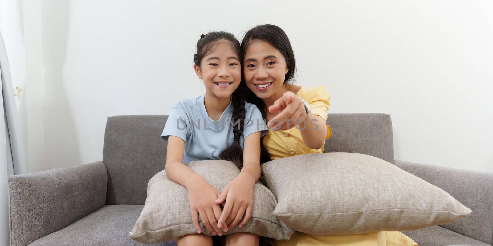 Excited young Asian mother and little girl watching television programs. Lifestyle and spends leisure at home