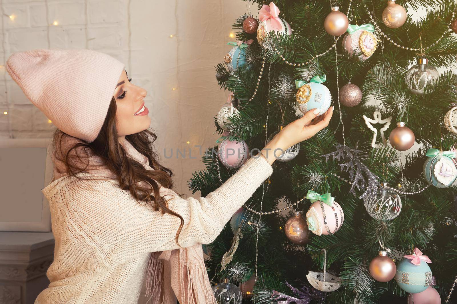 Happy young woman decorates the Christmas tree. Girl in a sweater decorating a Christmas tree with balls. New year and christmas holiday concept