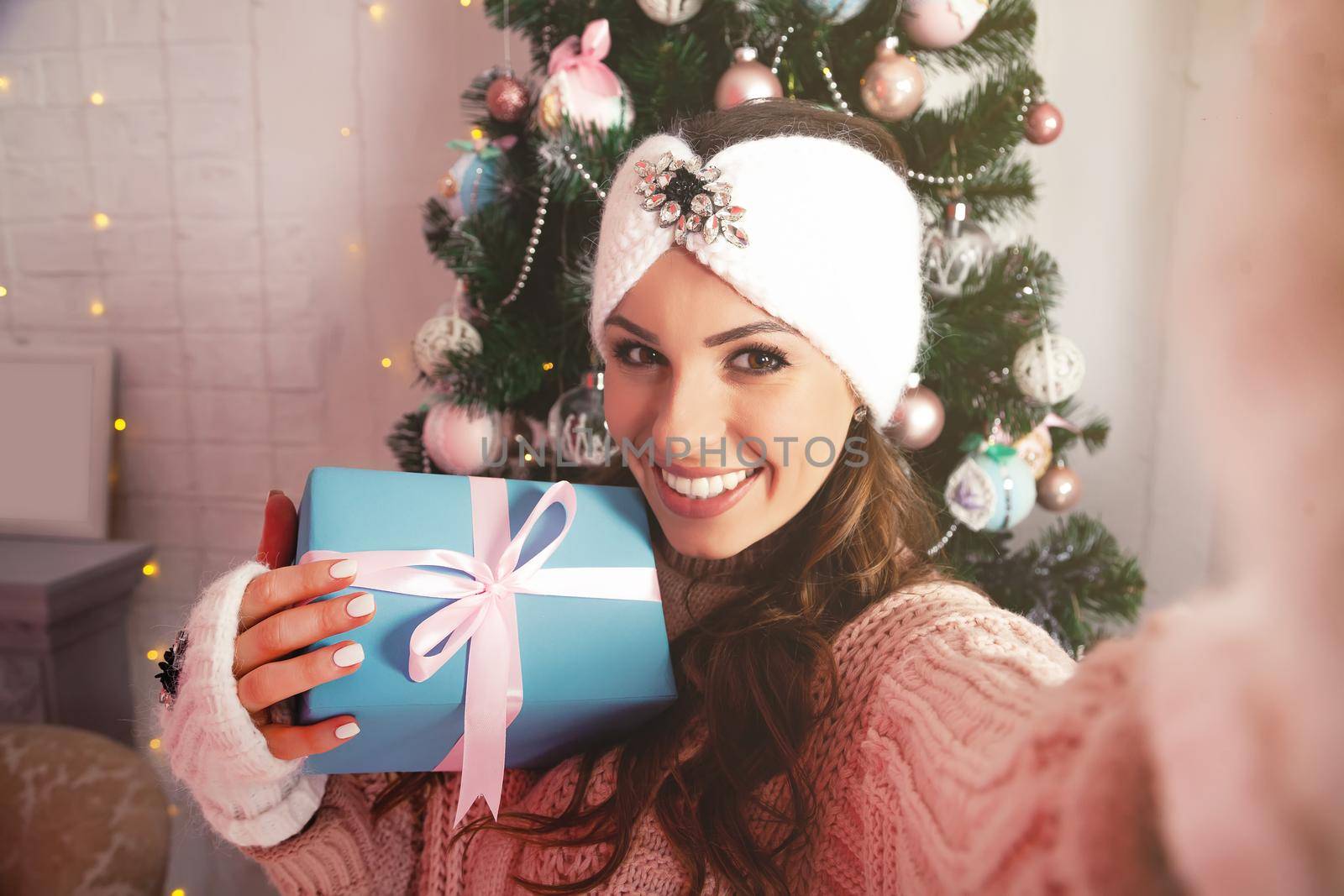 Self-portrait of a cheerful rejoicing girl removing a gift box with a Christmas tree behind her back. Young woman in winter clothes makes a photo with a gift for New Year and Christmas