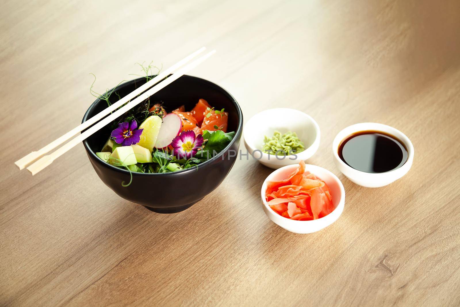 Poke salad with salmon in a bowl next to wasabi and ginger. Ingredients fresh salmon, avocado, cucumber, rice, Tamarind sauce mango sauce nori lime, sesame seeds, cilantro. Asian seafood salad concept