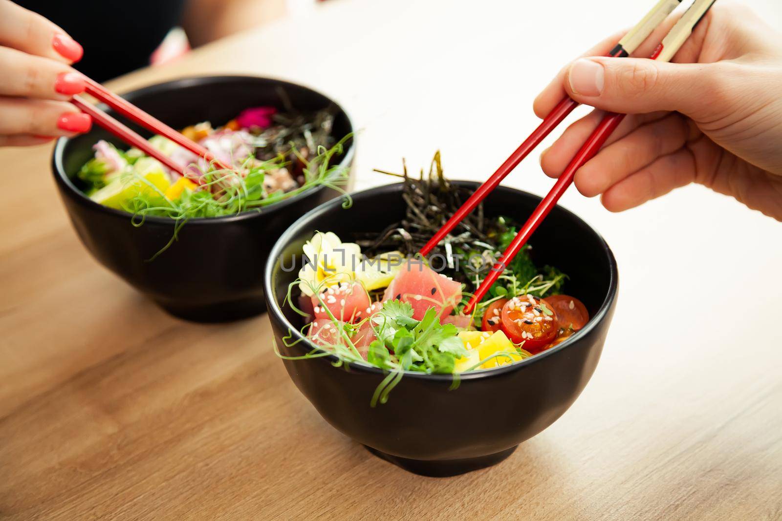 Man and woman eating poke salad with chopsticks. Dab tuna salad in a bowl. People in the restaurant eat salad with chopsticks. Asian seafood salad concept