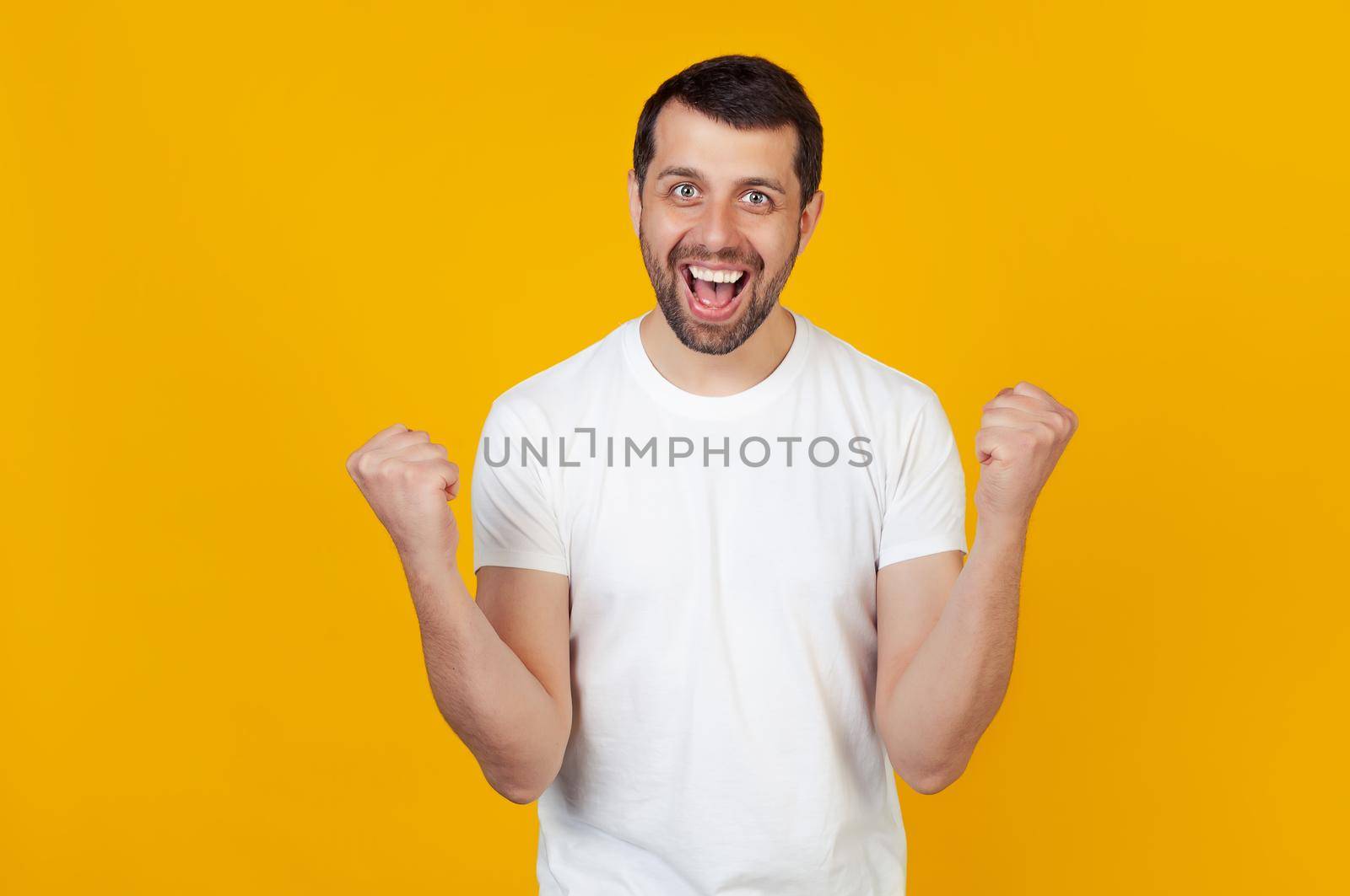 I won. Victory of success. Happy man celebrates being a winner. Dynamic image of a caucasian guy with a beard on a yellow studio background. Victory, delight concept. The concept of human emotions.
