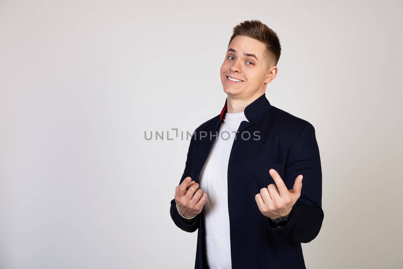 A young man, a handsome guy beckons to him with a finger. Come closer twitching a finger, beckons to come up to him, standing on a white background looks at the camera.