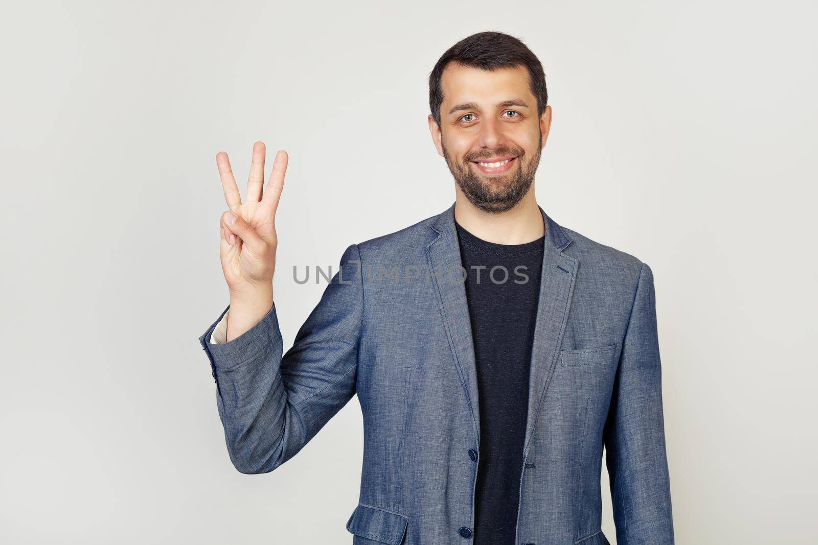 Young businessman with a beard smiles, male businessman in a stylish jacket showing the number three with his fingers, smiling confidently and happy looking at the camera