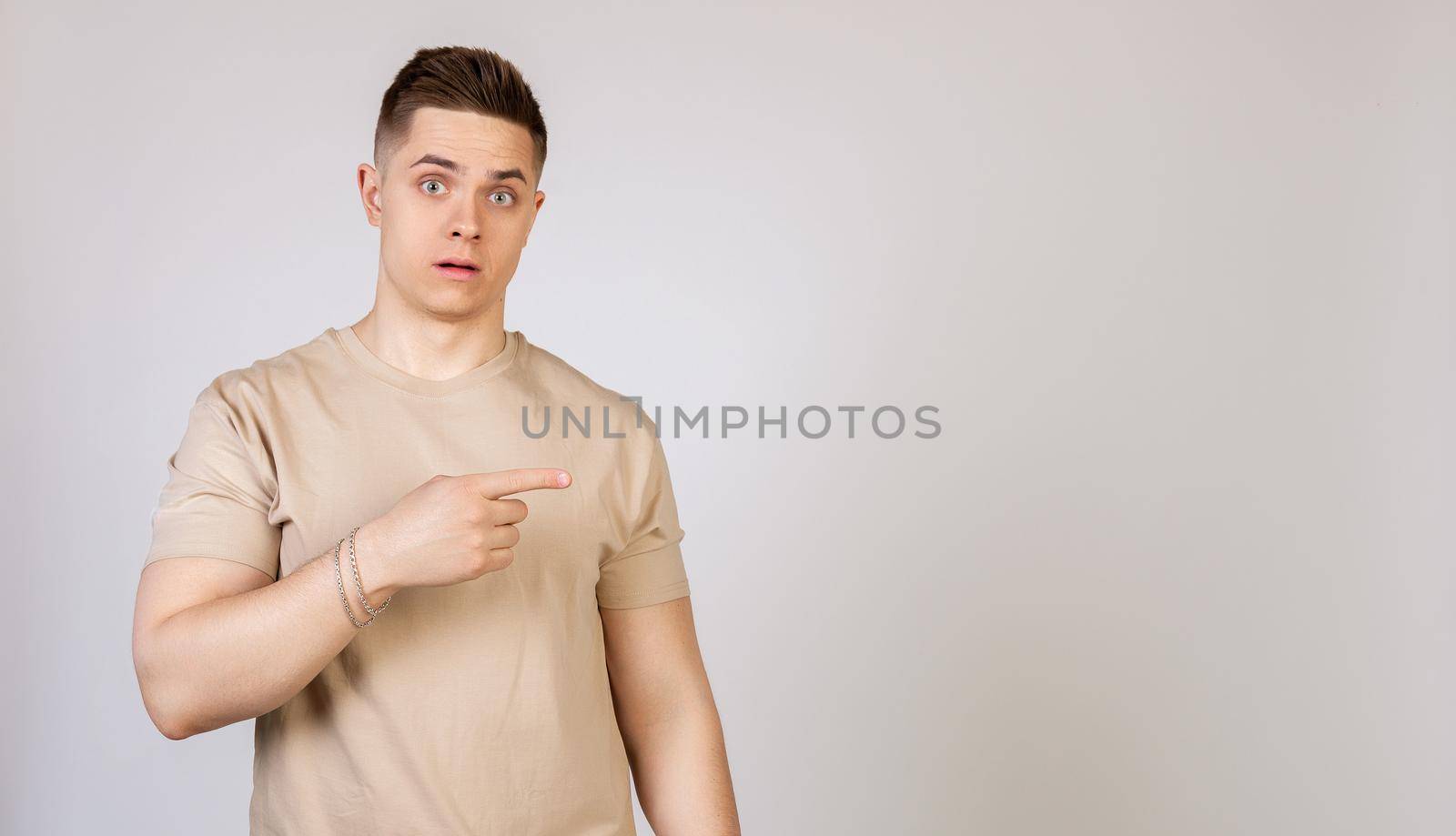 The man the guy points to the side with a displeased face. Young doubter man, holds his hand and points to the side with forefingers at blank space