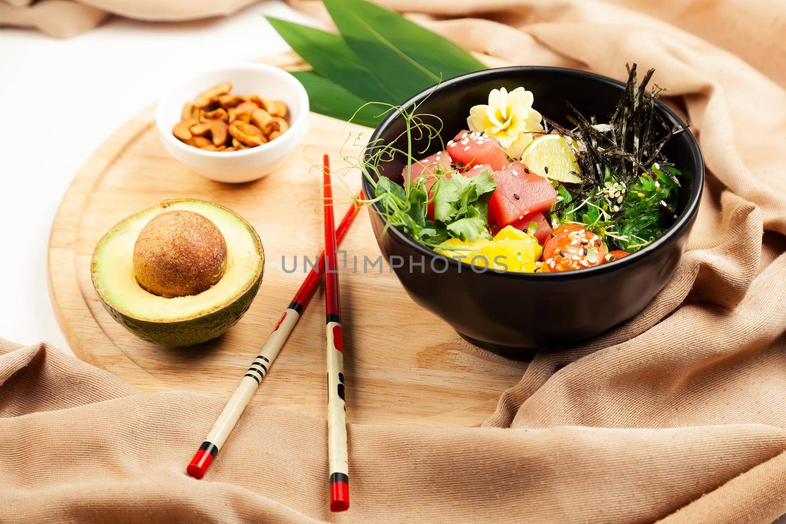 Poke salad with tuna in a bowl. Ingredients fresh tuna, cherry tomatoes, marinated seaweed, rice, takuan, Ponzu sauce, Teriyaki sauce, nori, sesame seeds, lime, cilantro. Asian seafood salad concept