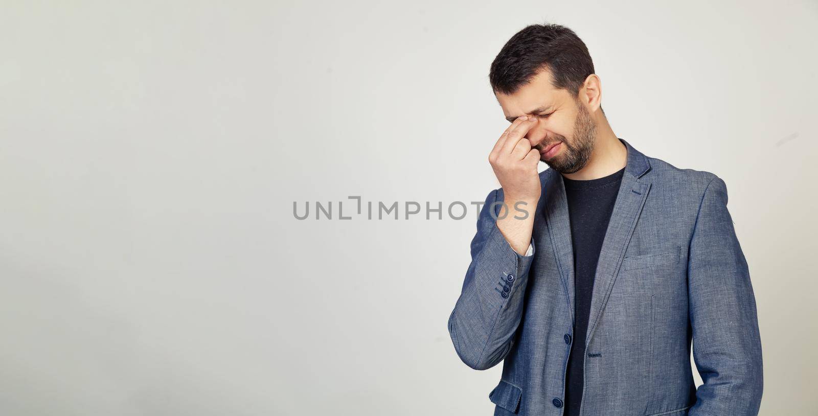 Young businessman man with a beard in a jacket, tired of rubbing his nose and eyes, feeling tired and headache. Stress and frustration concept. Portrait of a man on a gray background.
