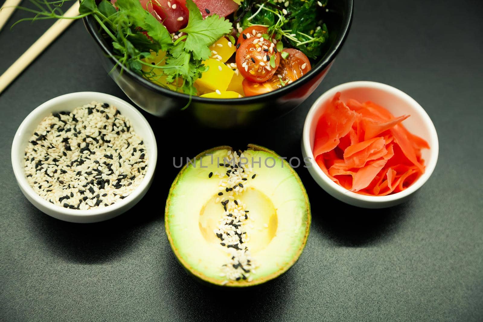 Poke salad with tuna in a bowl. Ingredients fresh tuna, cherry tomatoes, marinated seaweed, rice, takuan, Ponzu sauce, Teriyaki sauce, nori, sesame seeds, lime, cilantro. Asian seafood salad concept