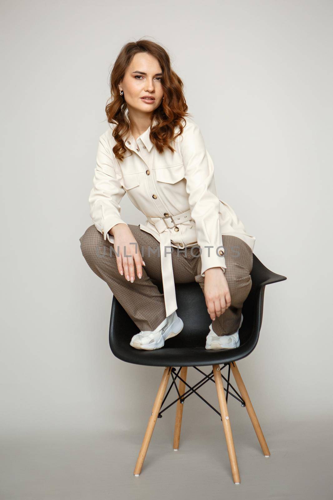 A model in a brown dress suit on a studio background. The girl next to the chair.