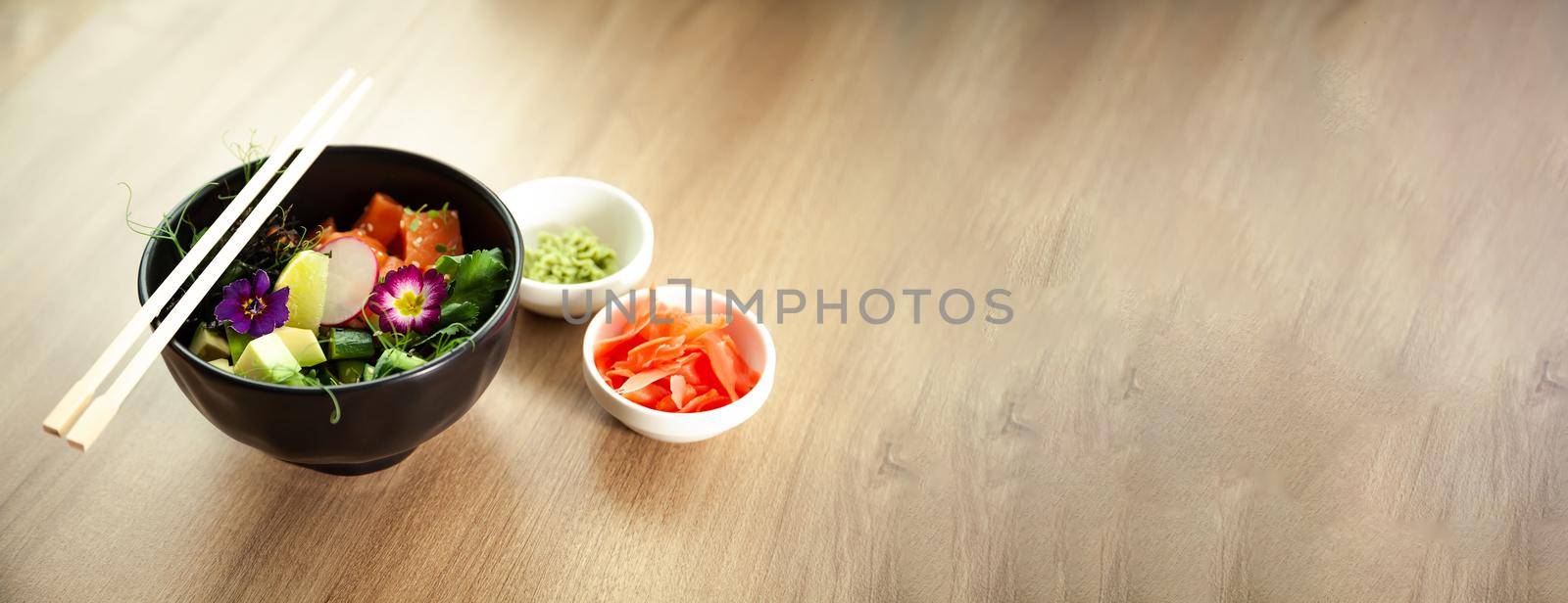 Poke salad with salmon in a bowl next to wasabi and ginger. Ingredients fresh salmon, avocado, cucumber, rice, Tamarind sauce mango sauce nori lime, sesame seeds, cilantro. Asian seafood salad concept