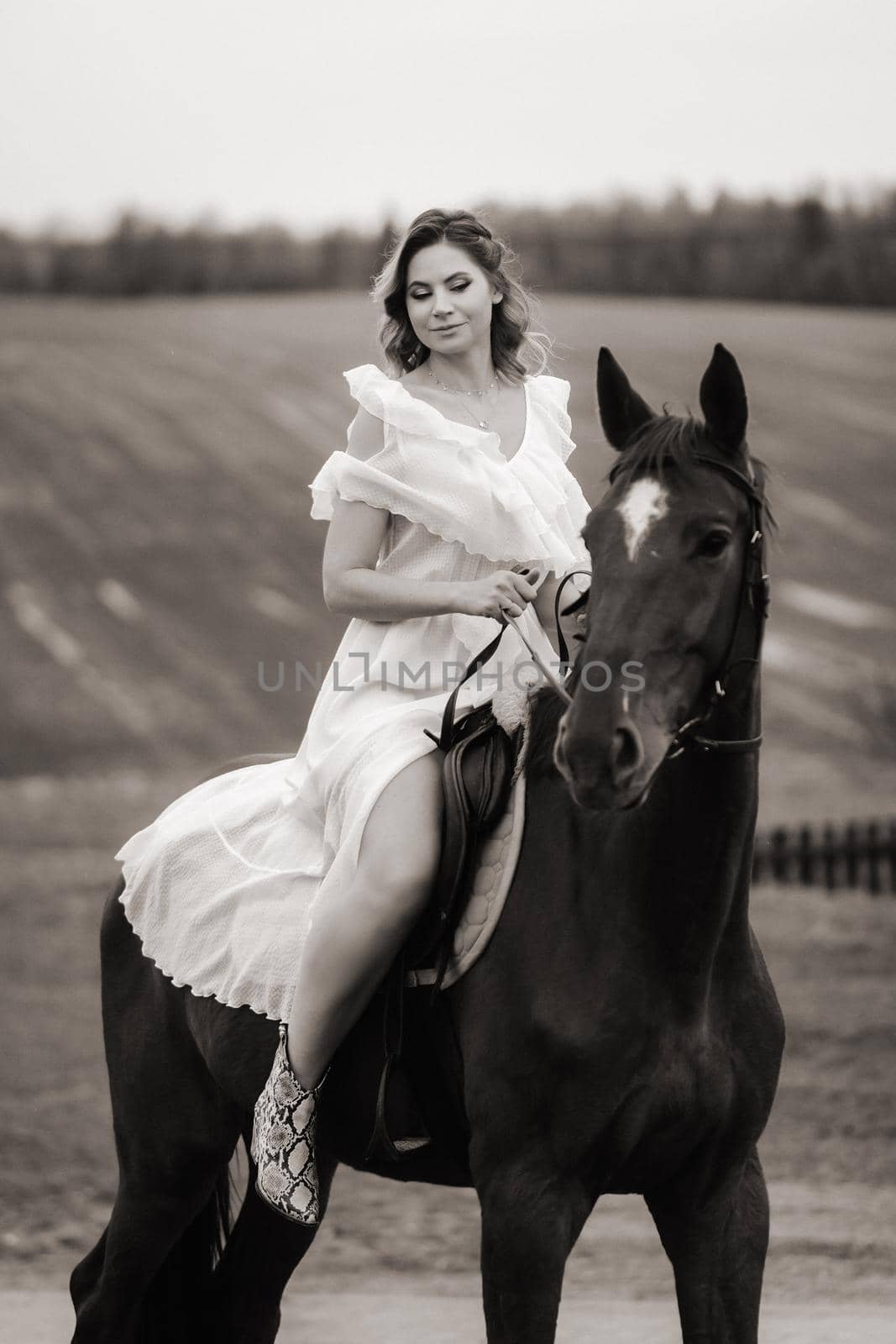A woman in a white sundress riding a horse in a field. black and white photo.