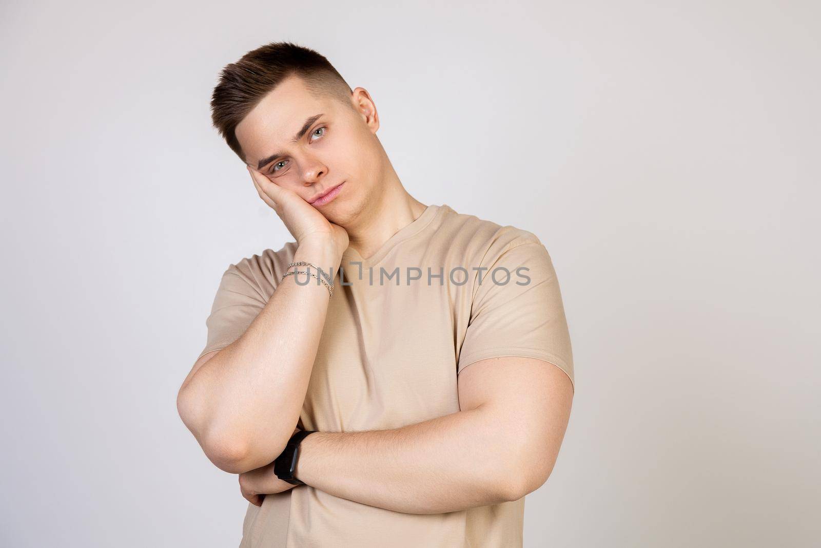 Young handsome guy holding his head with his hand, tired after a long and hard working day, standing on a white background looking at the camera.