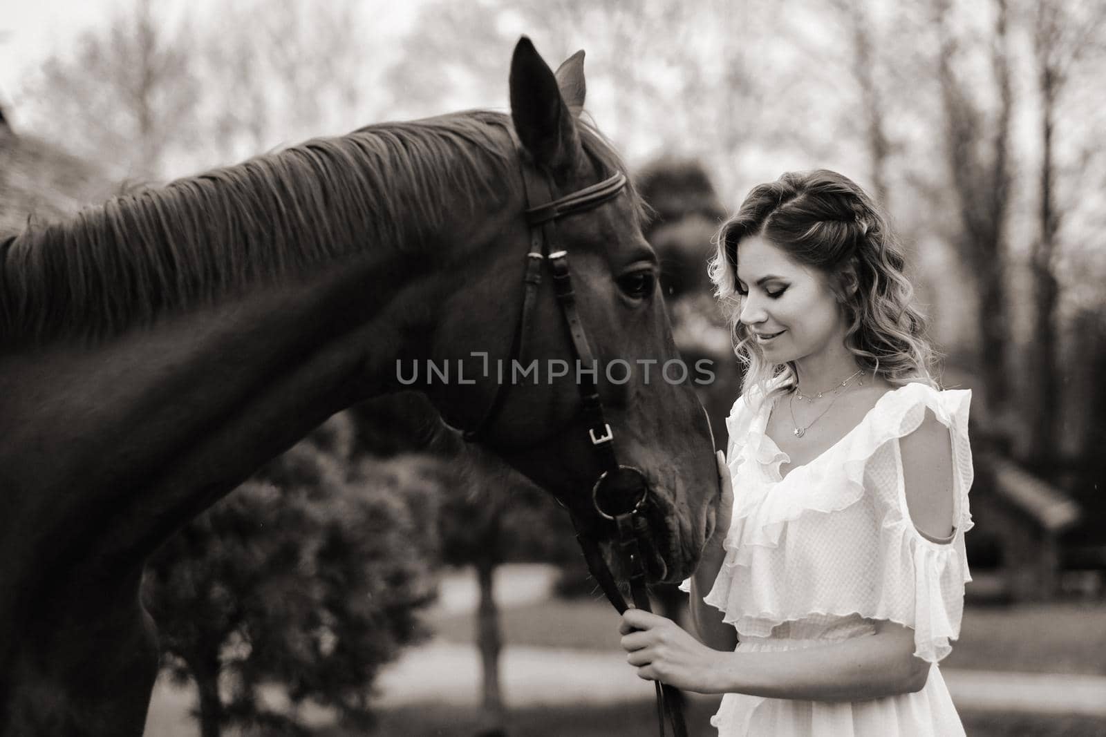 Beautiful girl in a white sundress next to a horse on an old ranch. black and white photo.