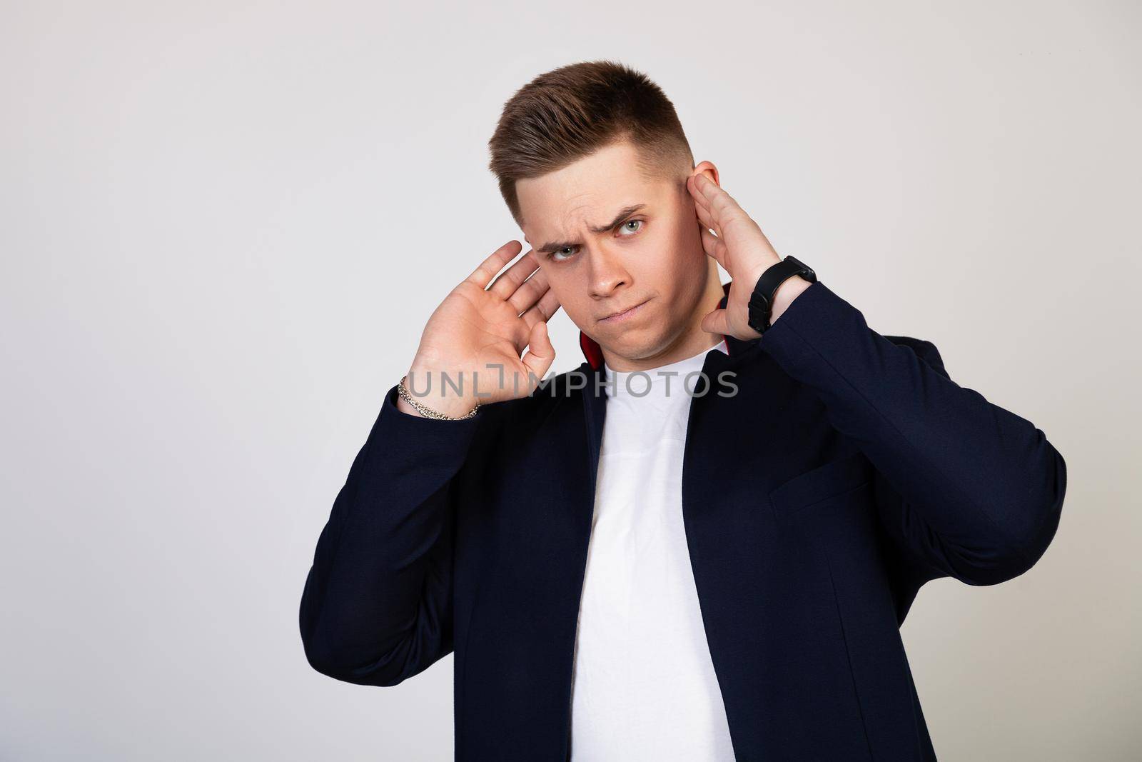 A young man covering his ears with his hands, he does not want to listen to news, gossip, information. Bearing terrible pain. Young guy covered his ears with his hands so as not to hear rumors.