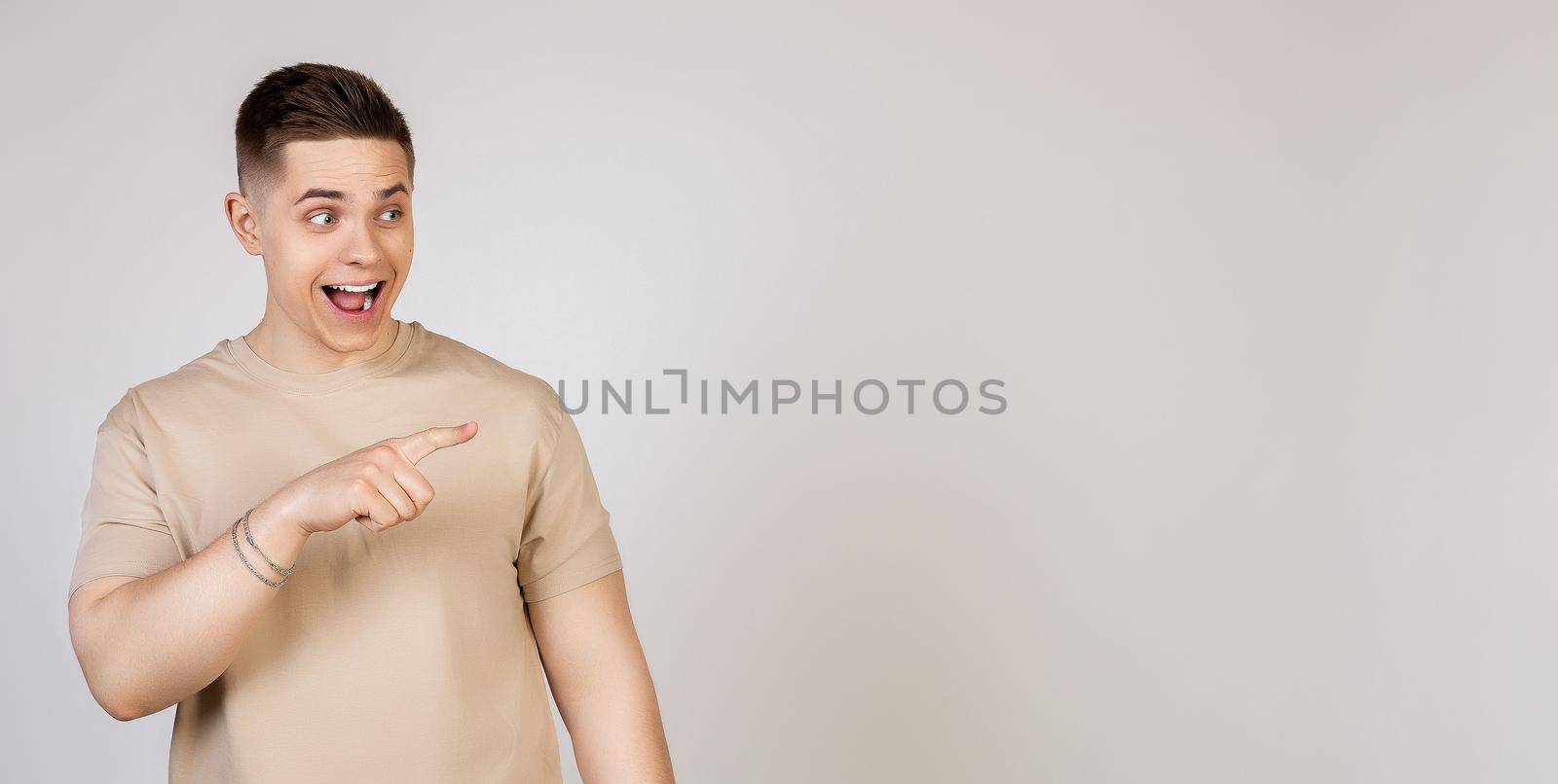 The man points to the side and smiles. Photo of young attractive excited handsome modern freelancer, entrepreneur, employer student looking at camera, pointing with index finger to copy space.