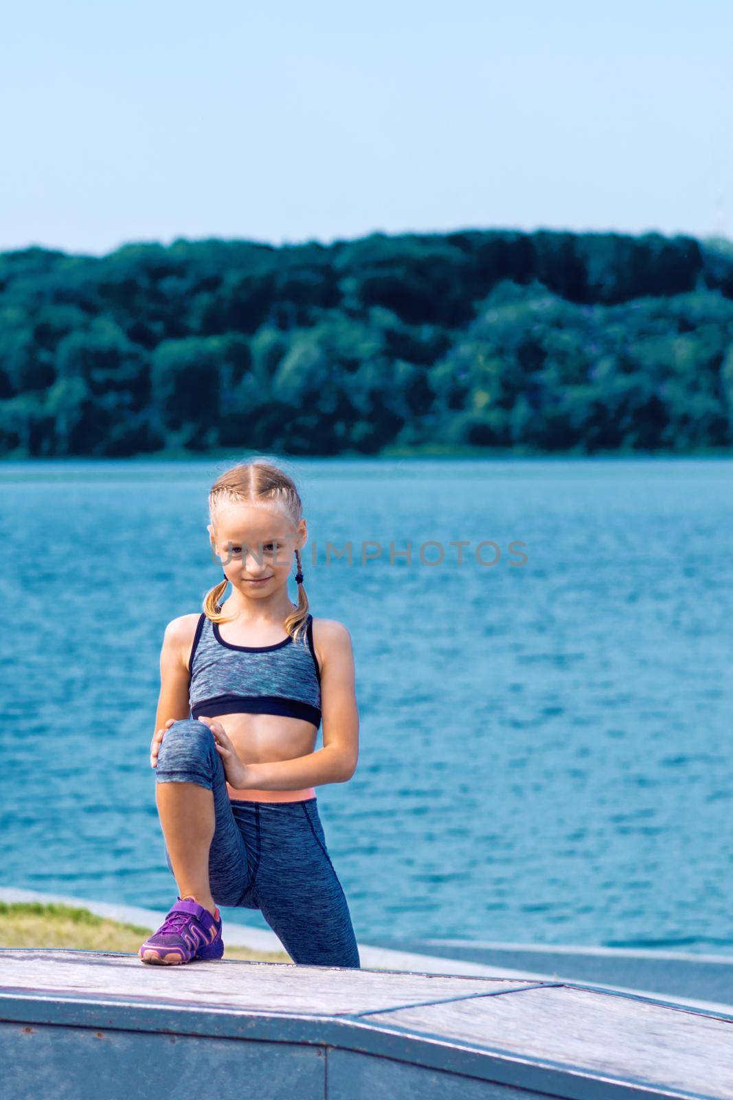 Portrait of little girl in sport style clothes by the lake in summer.