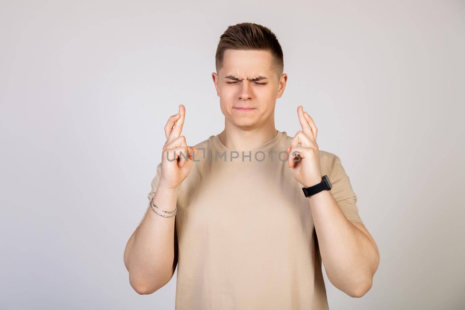 Photo of a young, nervous, excited man with his fingers crossed. Man holding fingers crossed with worried facial expression.