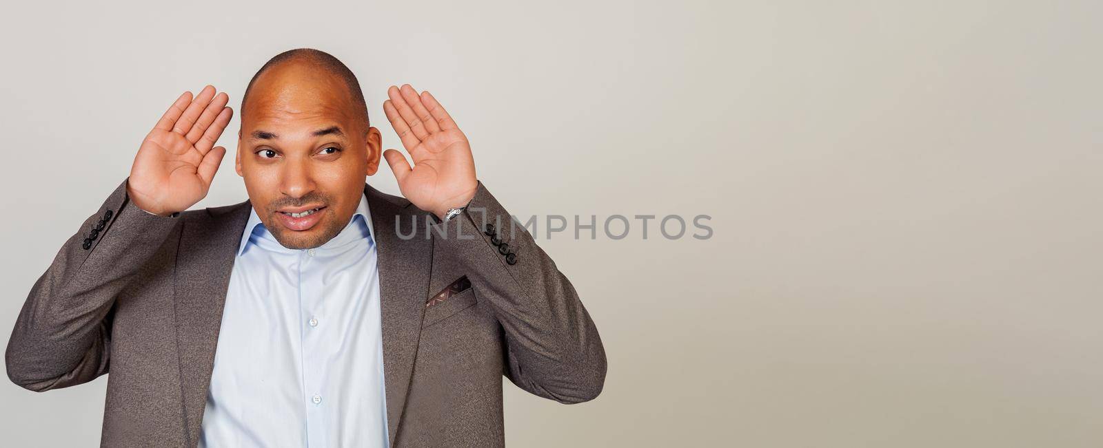 Man African American businessman, holding his hand behind his ear, showing that he does not hear, trying to listen to gossip, listen carefully to someone else's conversation.