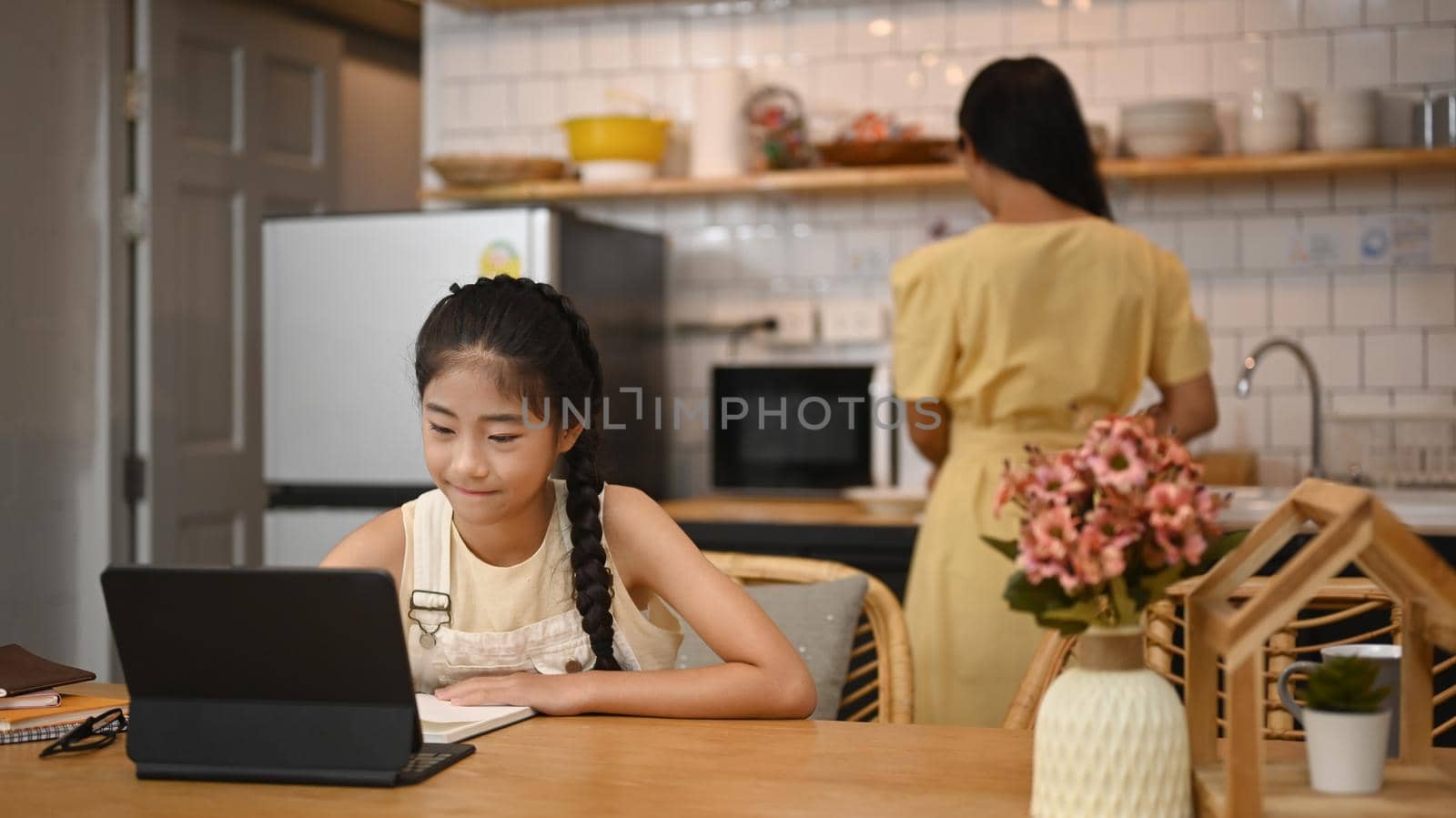 Focused little asian girl watching video lesson on computer laptop, interested in online web virtual class studying from at home. Homeschooling concept.