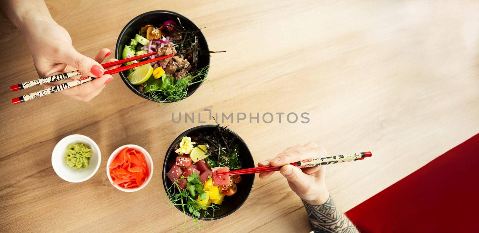 Loving couple man and woman eating salad poke chopsticks. Place the tuna salad in a bowl. People in the restaurant eat salad with chopsticks. Asian seafood salad concept