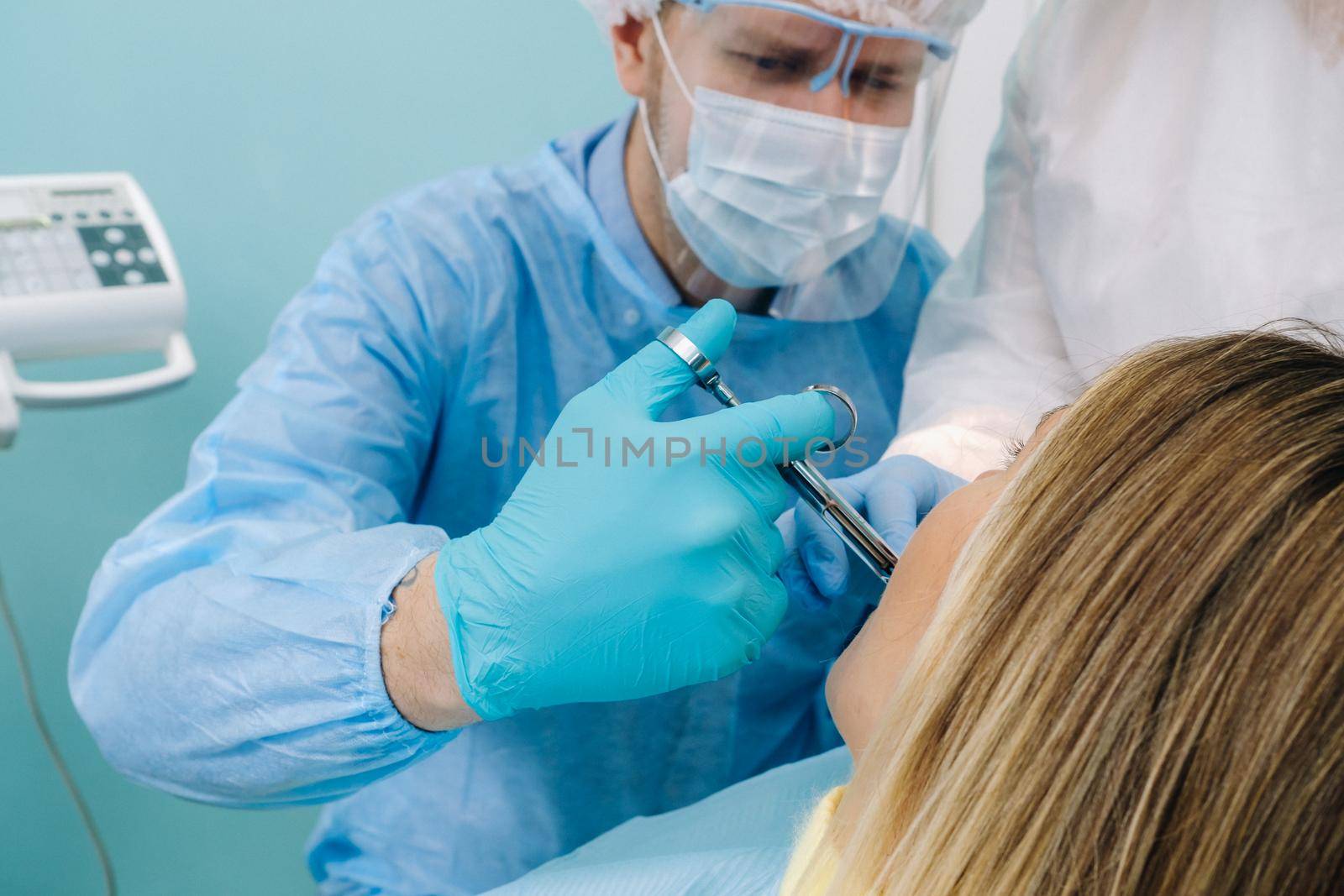 a dentist wearing a protective mask sits nearby and holds instruments in his hands before treating a patient in the dental office by Lobachad