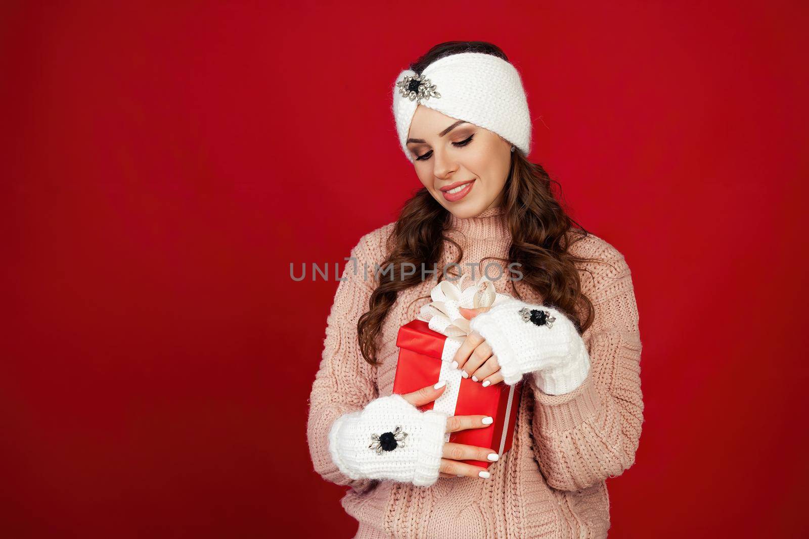 Happy young woman with a present, opening a Christmas present box. Portrait of happy smiling girl opening gift box isolated on red background