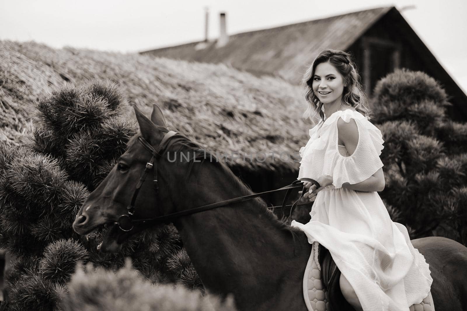 A woman in a white sundress riding a horse near a farm. black and white photo by Lobachad