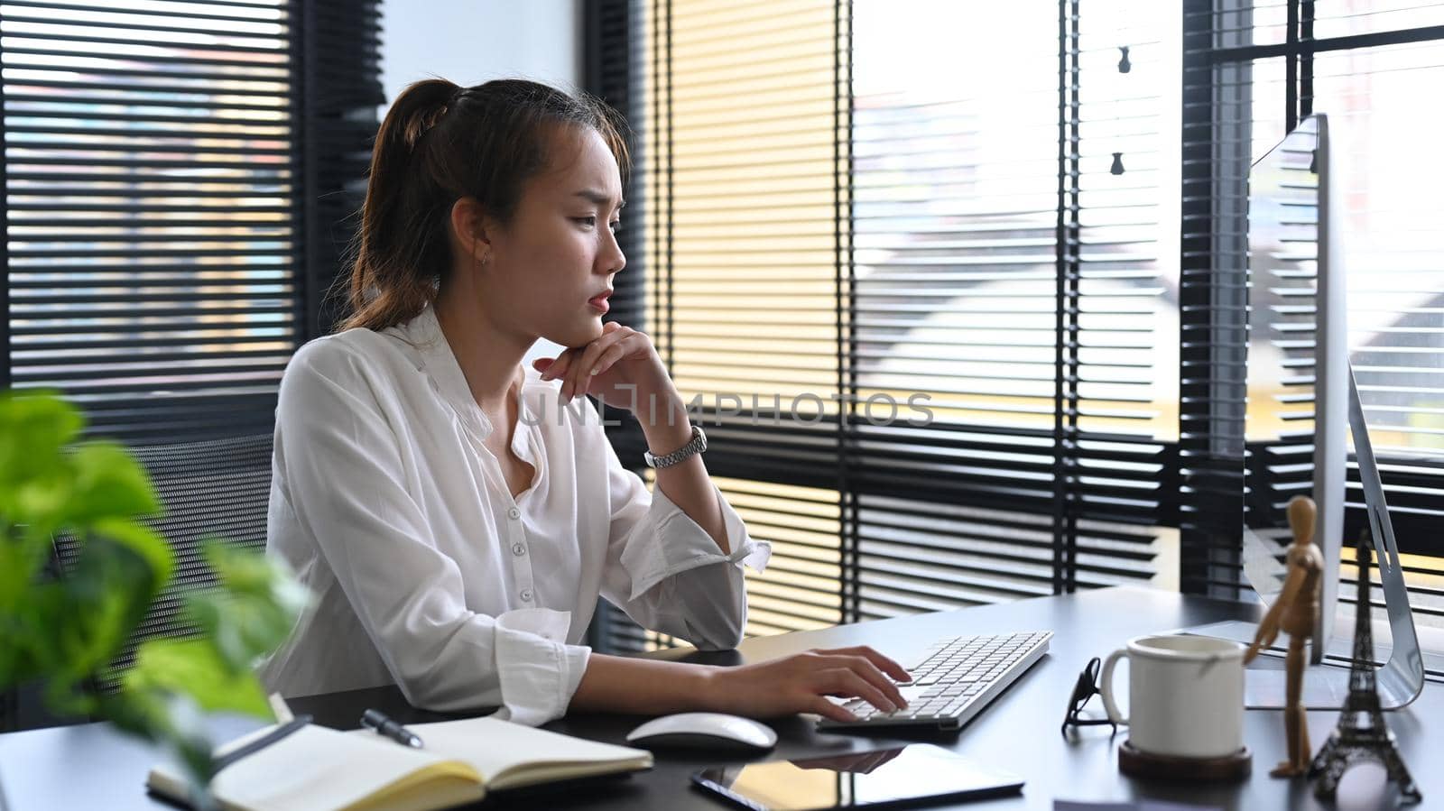 Thoughtful asian businesswoman looking at computer screen, analyzing financial data.