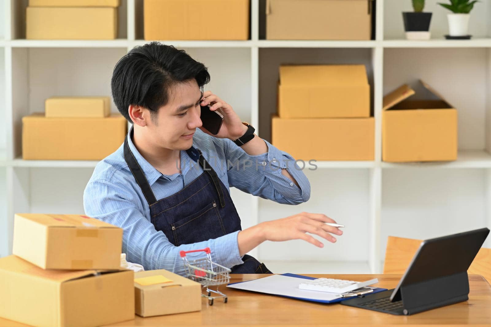 Young asian man talking on mobile phone for confirming orders from customer. Online selling, E-commerce concept.