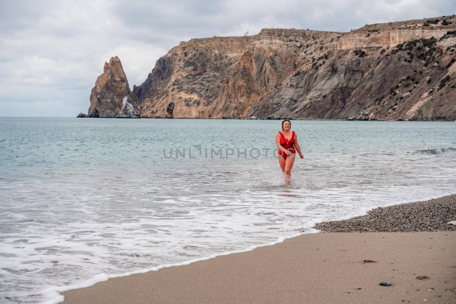 Woman in a bathing suit at the sea. A fat young woman in a red swimsuit enters the water during the surf.