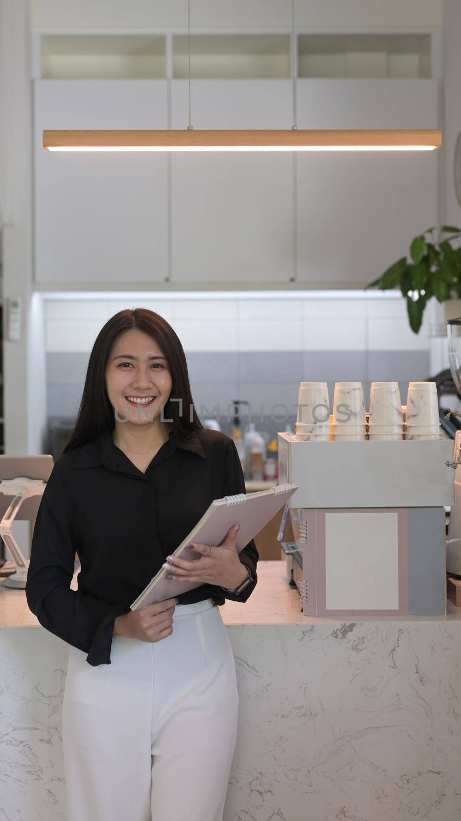 Portrait successful female business owner standing in front of counter at her coffee shop and smiling at camera.